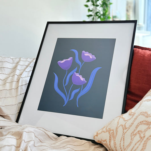 Framed art print on a bed featuring a gorgeous dark mystical themed floral print with wavy blue leaves and purple flowers.