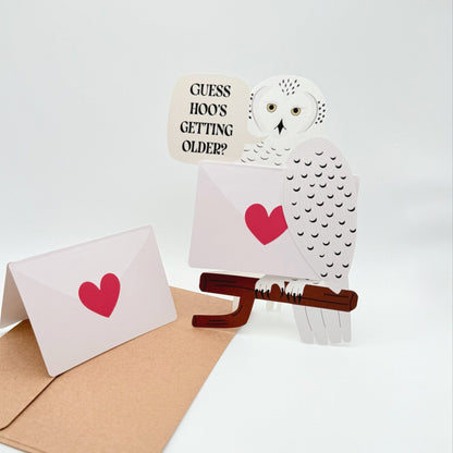 Cut out Snowy owl birthday card with pun ‘Guess hoo’s getting older'. A bird messenger holding a removable blank card 
