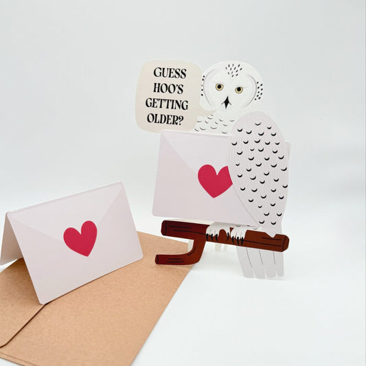 Cut out Snowy owl birthday card with pun ‘Guess hoo’s getting older'. A bird messenger holding a removable blank card 