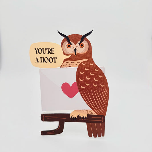 Funny die-cut owl greeting card with the pun “You’re a Hoot.” Great horned owl carrying a folded card, blank for message
